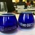 Two blue glass cups labeled 'International Culinary Center' and 'Olive Oil Times' on a table. - Olive Oil Times