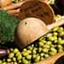 A collection of green olives displayed with wooden utensils and signs indicating prices. - Olive Oil Times