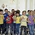 A group of children in colorful shirts singing together in a classroom setting. - Olive Oil Times