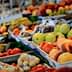 A selection of fresh fruits and vegetables displayed at a market stall, with a person holding a shopping list. - Olive Oil Times