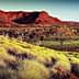 A red rock formation surrounded by grassland and sparse trees under a clear sky. - Olive Oil Times