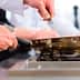 Chef in a white shirt using a frying pan on a gas stove in a kitchen setting. - Olive Oil Times