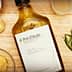 Bottle of olive oil labeled 'Pot d'Huile' with garlic, mustard, and herbs on a wooden surface. - Olive Oil Times