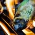 Green peppers being grilled on a barbecue grill with flames visible. - Olive Oil Times