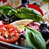 A bowl of mixed salad featuring cherry tomatoes, black olives, and fresh basil leaves. - Olive Oil Times