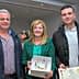 Three individuals posing with awards and a certificate at an event. - Olive Oil Times