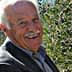 Elderly man smiling while standing next to olive trees with ripe olives. - Olive Oil Times