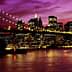Brooklyn Bridge illuminated at night with the New York City skyline in the background under a purple sky. - Olive Oil Times