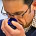 A man wearing glasses and a checkered shirt smelling olive oil from a blue glass cup. - Olive Oil Times