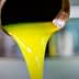 Golden olive oil pouring from a metal spout into a container. - Olive Oil Times