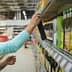 A woman reaching for a bottle of olive oil on a grocery store shelf filled with various products. - Olive Oil Times