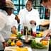 Three chefs in a culinary class preparing ingredients with fruits and vegetables on a table. - Olive Oil Times