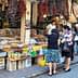 A market scene featuring various spices and dried goods displayed on tables with shoppers interacting. - Olive Oil Times