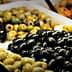 Assorted olives in various colors and sizes displayed in baskets with serving utensils. - Olive Oil Times