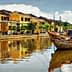Traditional wooden boats moored on a river with reflections of buildings in Hoi An, Vietnam. - Olive Oil Times