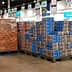 Pallets of stacked boxes in a retail store aisle with employees nearby. - Olive Oil Times