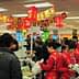Crowd of shoppers and cashiers at a busy supermarket checkout area with red decorations. - Olive Oil Times