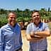 Two men standing in an olive grove, smiling and posing for the camera. - Olive Oil Times