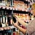Woman inspecting a bottle of olive oil in a grocery store aisle filled with various products. - Olive Oil Times