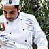 Chef in a white uniform with a hat pouring olive oil from a container. - Olive Oil Times