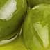 Three green olives placed in a small dish with olive oil. - Olive Oil Times