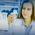 Female scientist examining a beaker containing a liquid in a laboratory setting. - Olive Oil Times