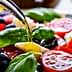 Fresh salad with tomatoes, mozzarella, olives, and basil being drizzled with olive oil. - Olive Oil Times