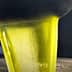 Stream of green olive oil being poured from a metal container into a stainless steel surface. - Olive Oil Times