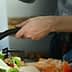 A person stirring food in a frying pan while preparing ingredients on a kitchen countertop. - Olive Oil Times