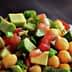 A close-up of a chickpea salad with diced avocado, tomatoes, and green onions in a white bowl. - Olive Oil Times