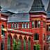 Historic red brick building featuring multiple towers and arched windows against a cloudy sky. - Olive Oil Times