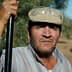 A man wearing a cap and glasses, holding a stick while standing in an olive grove. - Olive Oil Times