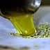 Stream of green olive oil pouring from a metal spout onto a surface. - Olive Oil Times