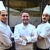 Three chefs wearing white uniforms and hats standing in front of a restaurant entrance. - Olive Oil Times
