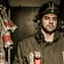 Firefighter wearing a helmet and uniform, standing in a storage area with hoses and equipment in the background. - Olive Oil Times