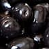 A close-up view of shiny black olives piled together in a cluster. - Olive Oil Times