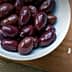 Bowl of Kalamata olives next to feta cheese on a wooden cutting board. - Olive Oil Times