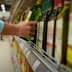A person reaching for a bottle of olive oil on a supermarket shelf. - Olive Oil Times