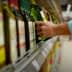 A person reaching for a green bottle of olive oil on a supermarket shelf. - Olive Oil Times