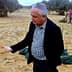 Man in a black jacket holding sand in his hand in an olive grove with a woman in the background. - Olive Oil Times