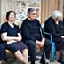 Six elderly women dressed in black and gray sitting on a bench in a casual setting. - Olive Oil Times