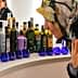 Woman wearing a floral headscarf examining various bottles of olive oil on display. - Olive Oil Times