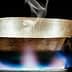 Metal cooking pan with steam rising above it on a gas stove with a blue flame. - Olive Oil Times