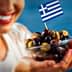 A woman smiling while holding a bowl of assorted olives topped with a small Greek flag. - Olive Oil Times