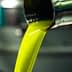 Golden green olive oil pouring from a metal spout in a production facility. - Olive Oil Times