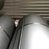 Several large silver storage tanks stacked closely together in a warehouse setting. - Olive Oil Times