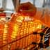 A person holding a bottle of cooking oil on a production line with multiple bottles in the background. - Olive Oil Times