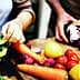 Hands preparing vegetables including lettuce, carrots, tomatoes, and cabbage on a wooden cutting board. - Olive Oil Times