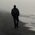 Individual walking alone on a foggy beach with gentle waves lapping at the shore. - Olive Oil Times