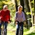 A man and woman riding bicycles side by side on a tree-lined path during daylight. - Olive Oil Times